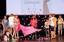 Foto von Schülerinnen, die ein rosa Tuch mit Papierblumen in die Luft werfen