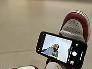 Foto von einem Handy im Selfie-Modus, das auf einem Fuß balanciert wird und am Display eine Schülerin in Pose zeigt