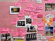 Foto einer Wand, die mit rosa Papier überzogen ist und auf der Fotos und beschriftete Post-Its hängen