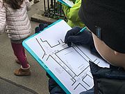 Foto von zwei Schülern auf Stadtexkursion, die im Freien mit einem Klemmboard, einem Plan und einem Bleistift arbeiten